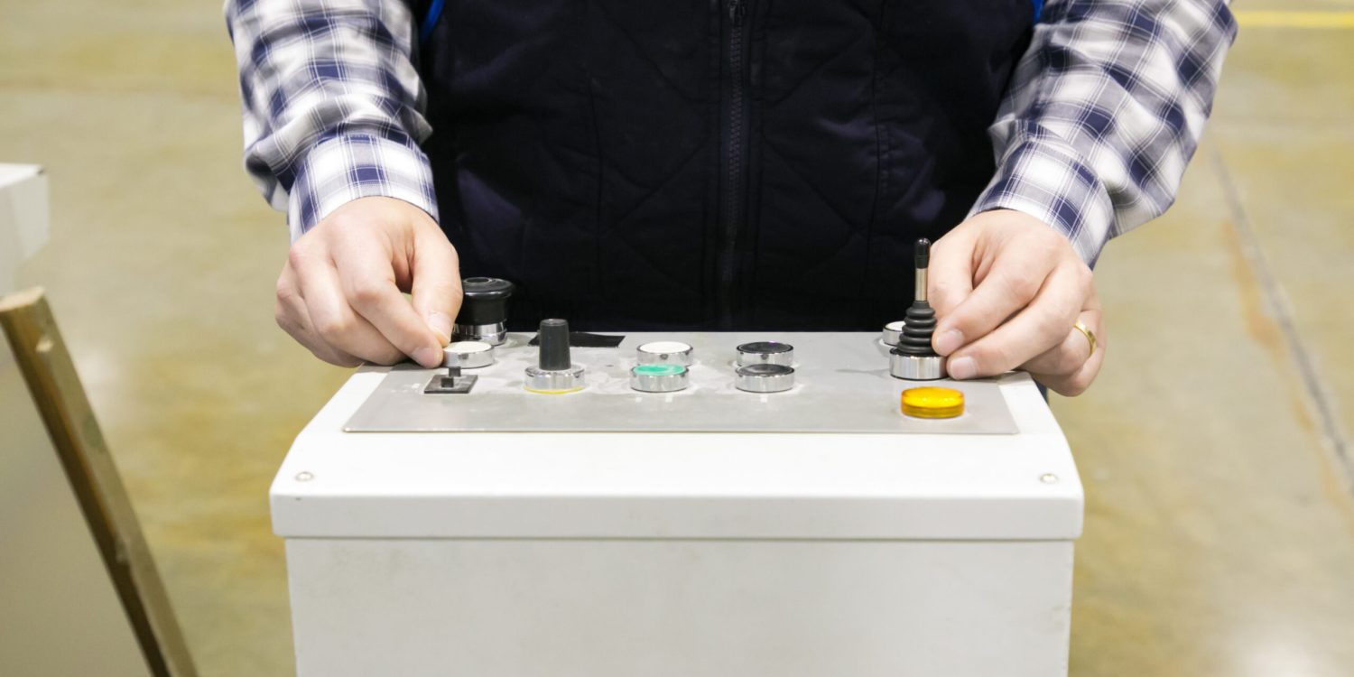 Cropped shot of factory machine operator pressing buttons at control panel. Hands of man working in vest and checkered shirt working at plant. Technology or production process concept